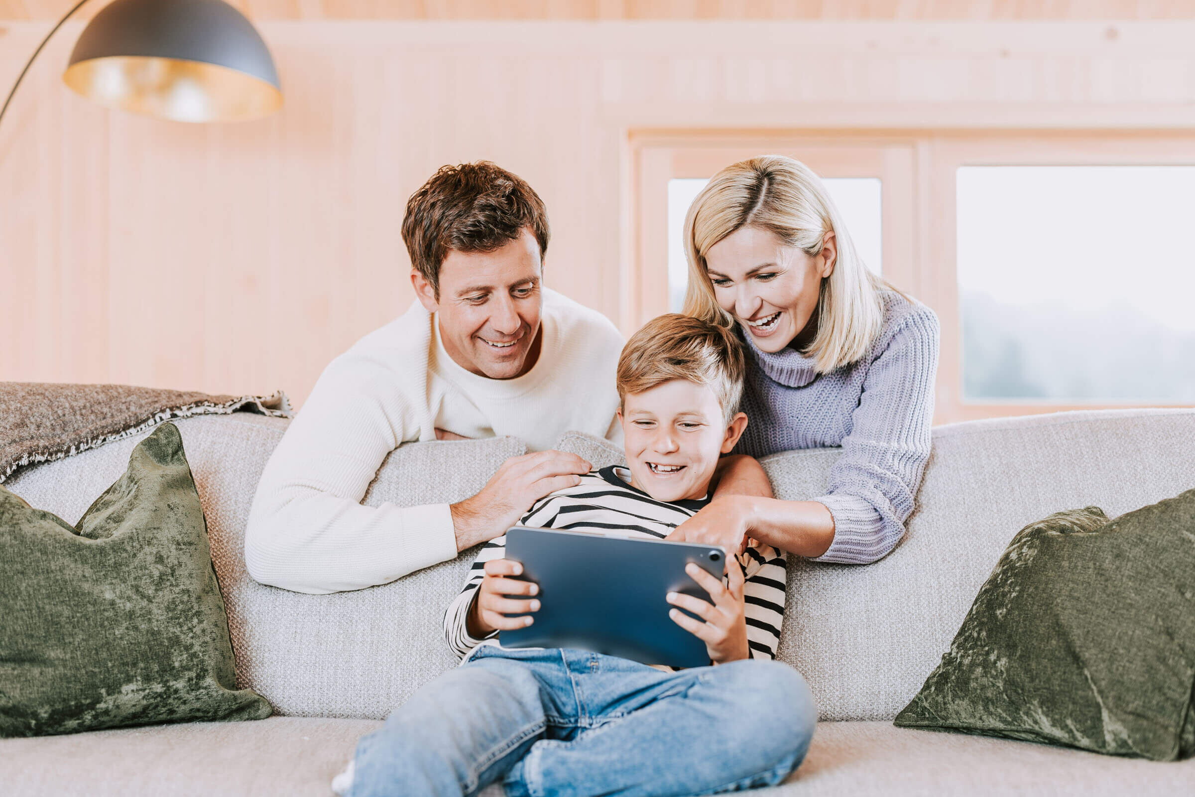 Familie sitzt in Wohnzimmer auf Sofa und spielt mit Tablet