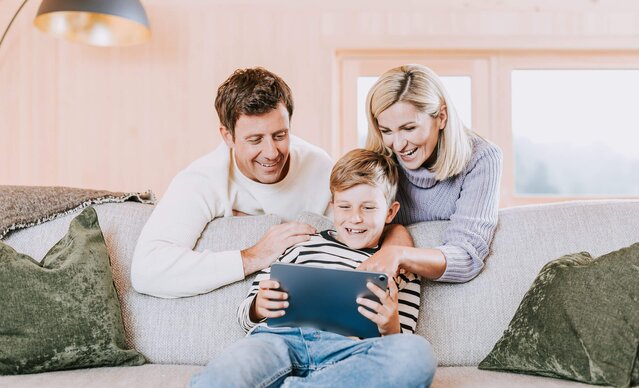 Familie sitzt in Wohnzimmer auf Sofa und spielt mit Tablet
