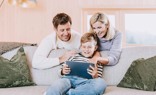 Familie sitzt in Wohnzimmer auf Sofa und spielt mit Tablet