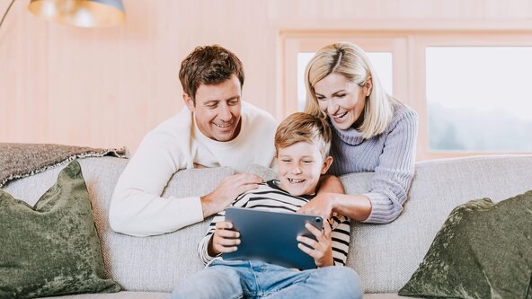 Familie sitzt in Wohnzimmer auf Sofa und spielt mit Tablet