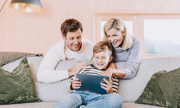 Familie sitzt in Wohnzimmer auf Sofa und spielt mit Tablet