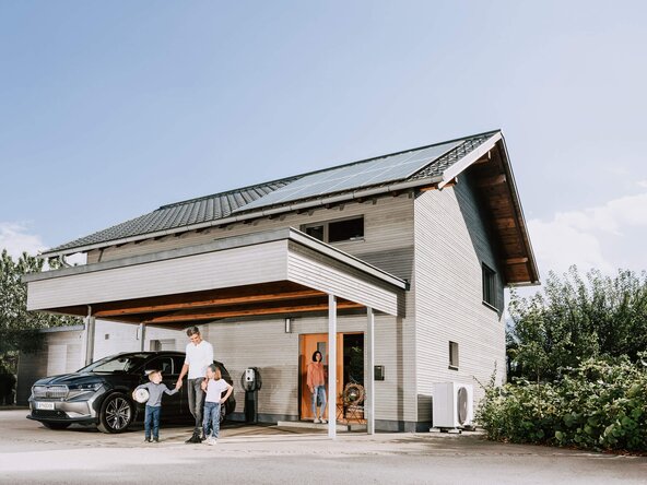 Familie steht vor Einfamilienhaus mit Photovoltaikanlage, Wärmepumpe und Wallbox