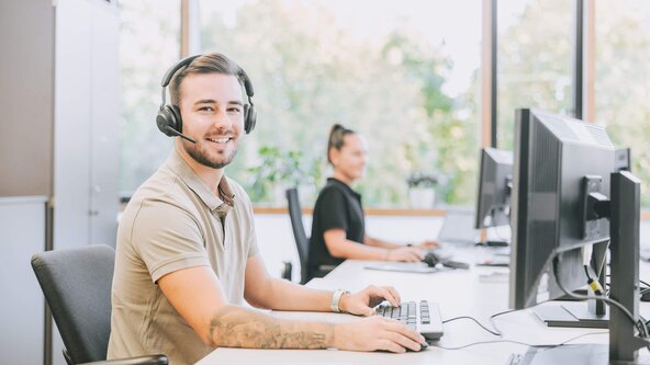 Kundenservicemitarbeiter mit Headset sitzt in offenem Büro