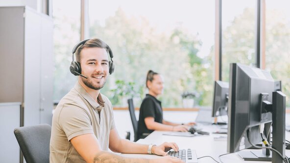Kundenservicemitarbeiter mit Headset sitzt in offenem Büro