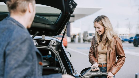 Mann schließt Kofferraumklappe während Frau ihr E-Auto lädt