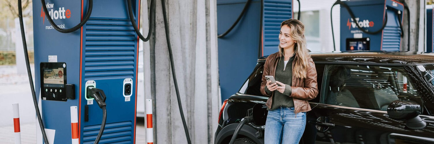 Frau lehnt sich an ihrem Auto an. während das Fahrzeug am Schnelllader auflädt