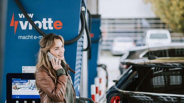 Junge Frau telefoniert, während ihr Fahrzeug am Schnelllader auflädt