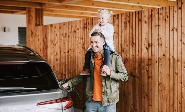 Mädchen sitzt auf den Schultern ihres Vaters, der sein E-Auto auflädt