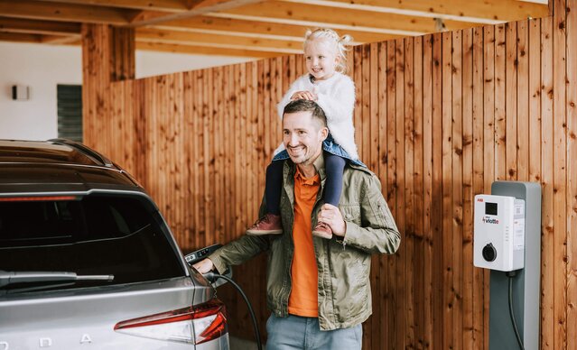 Mädchen sitzt auf den Schultern ihres Vaters, der sein E-Auto auflädt