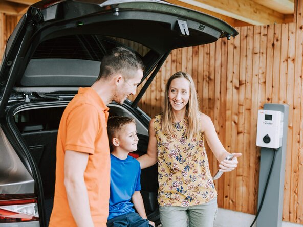 Familie sitzt im Kofferraum, während ihr E-Auto an der Wallbox auflädt