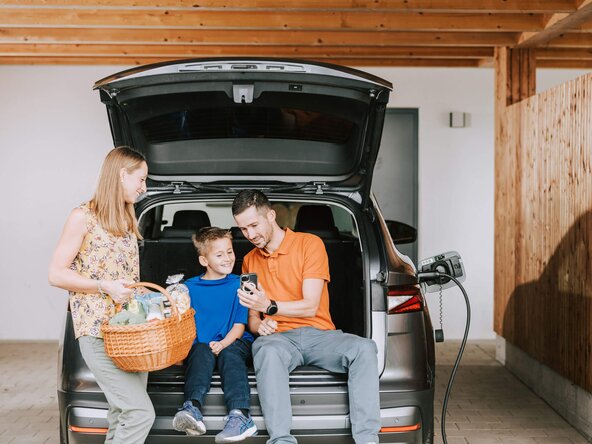 Familie sitzt im Kofferraum, während ihr E-Auto an der Wallbox auflädt