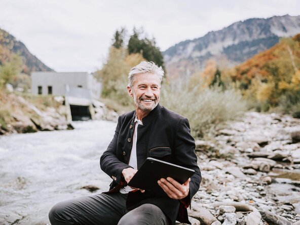Mann bedient Tablet in der Natur und steuert damit das Wasserkraftwerk