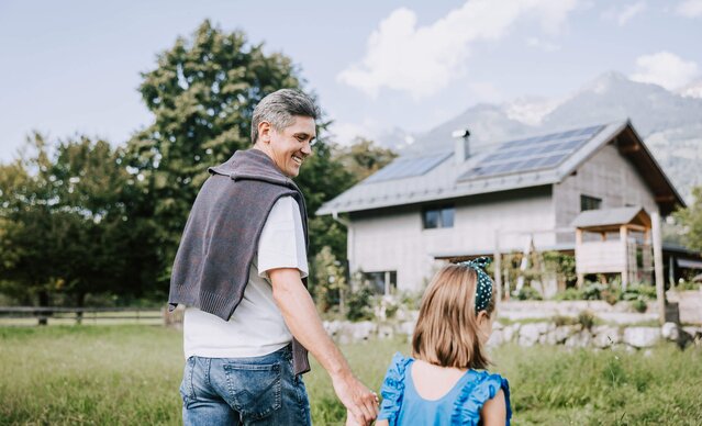 Vater und Tochter spazieren Richtung Einfamilienhaus mit PV Anlage