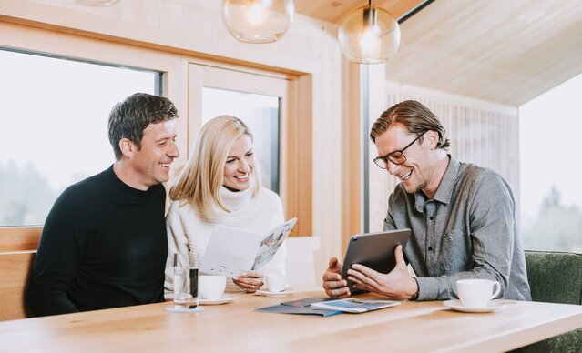 Energieberater sitzt bei Familie am Tisch und zeigt etwas auf dem Tablet