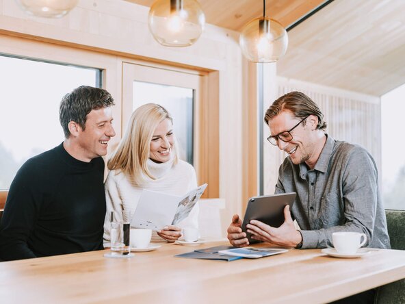 Energieberater sitzt bei Familie am Tisch und zeigt etwas auf dem Tablet