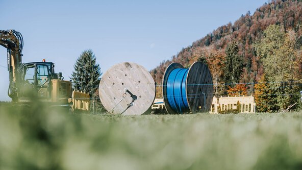 Zwei Glasfaserkabeltrommeln und ein Bagger stehen auf einer Wiese