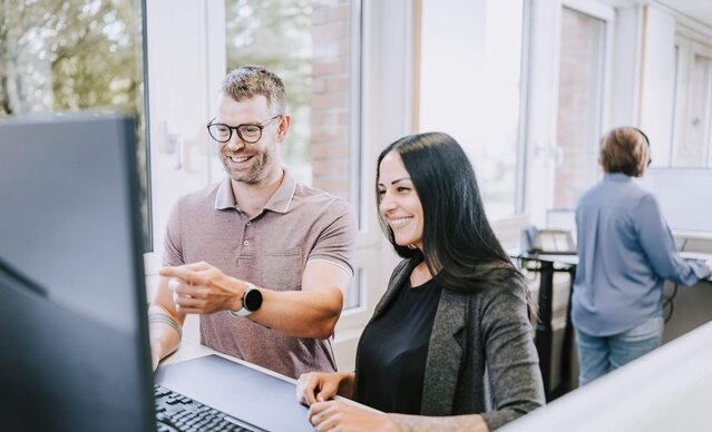 Zwei Kundenservicemitarbeiter sitzen vor dem Bildschirm und zeigen was