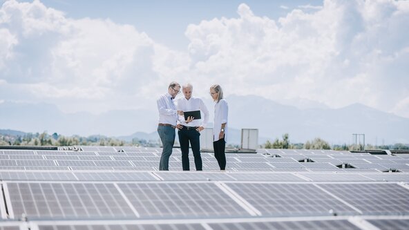 Drei Personen stehen auf dem Dach und begutachten die PV Anlage