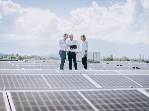 Drei Personen stehen auf dem Dach und begutachten die PV Anlage