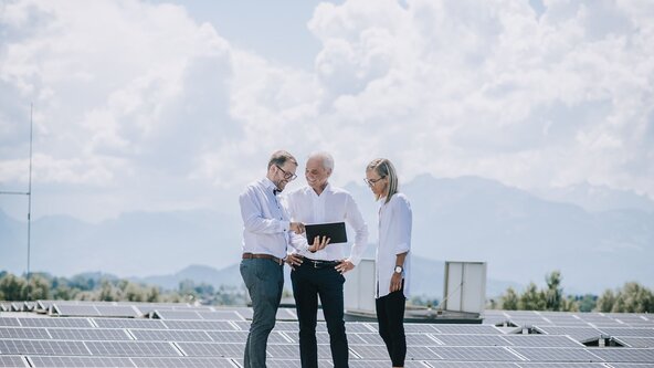 Drei Personen stehen auf dem Dach und begutachten die PV Anlage