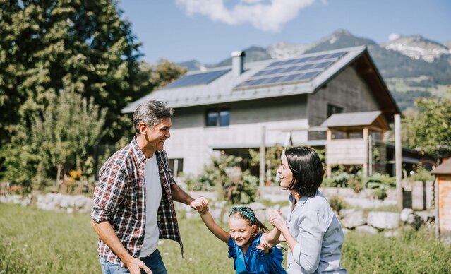 Familie spielt im Garten vor einem Haus mit PV Anlage