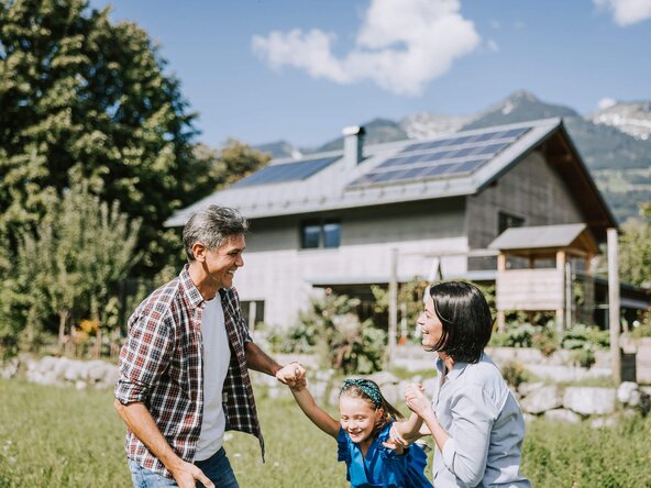 Familie spielt im Garten vor einem Haus mit PV Anlage