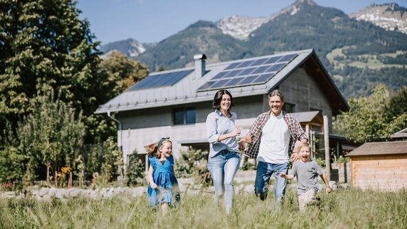 Familie läuft durch Wiese vor Haus mit PV Anlage