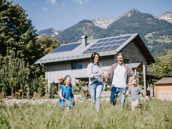 Familie läuft durch Wiese vor Haus mit PV Anlage