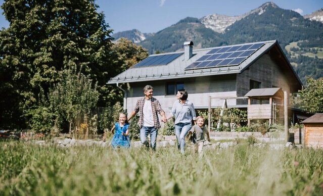 Familie läuft durch Wiese vor Haus mit PV Anlage