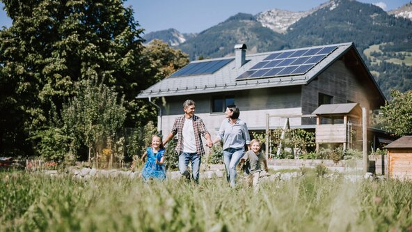 Familie läuft durch Wiese vor Haus mit PV Anlage