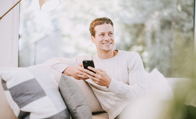 Mann mit Smartphone sitzt auf Couch
