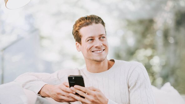 Mann mit Smartphone sitzt auf Couch