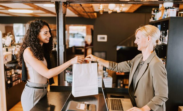 Ladenbesitzerin gibt Kundin eine weiße Tasche
