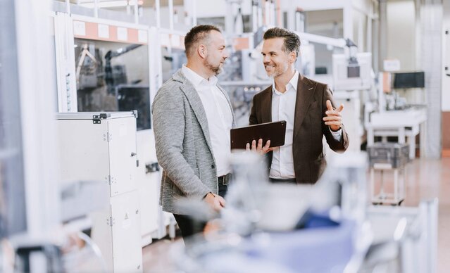 Kundenbetreuer führt Gespräch mit Unternehmer in Produktionshalle