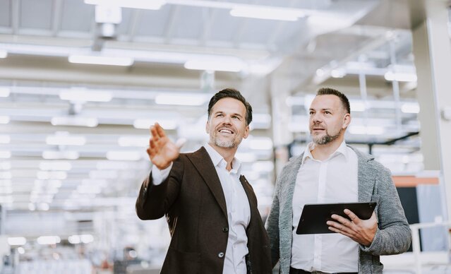 Kundenbetreuer führt Gespräch mit Unternehmer in Produktionshalle