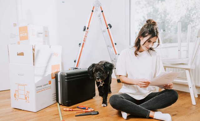 Frau sitzt im Schneidersitz auf dem Boden neben Umzugskartons