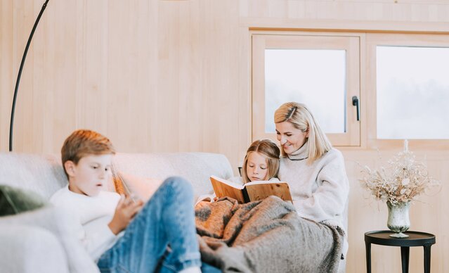 Mutter liest Tochter auf Sofa ein Buch vor, Sohn spielt am Handy