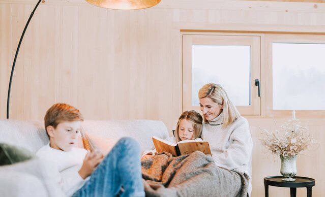 Mutter liest Tochter auf Sofa ein Buch vor, Sohn spielt am Handy