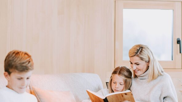 Familie sitzt gemütlich auf der Couch und liest ein Buch
