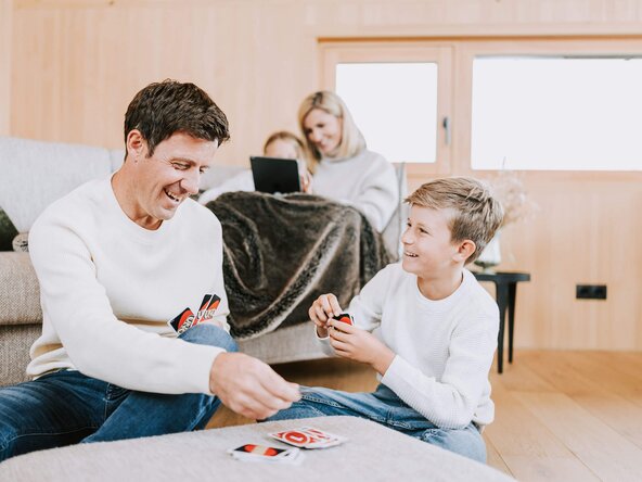 Vater und Sohn spielen UNO, während die Mutter der Tochter etwas auf dem Tablet zeigt