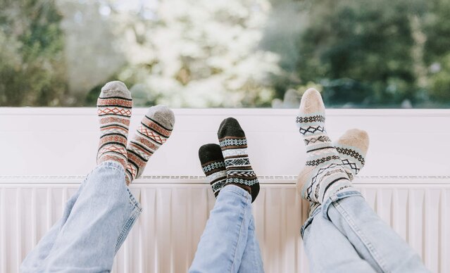 Drei paar Füße mit Wollsocken auf einem Heizkörper