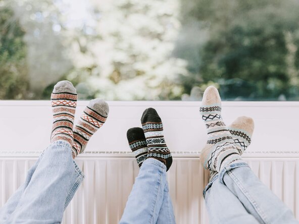 Drei paar Füße mit Wollsocken auf einem Heizkörper