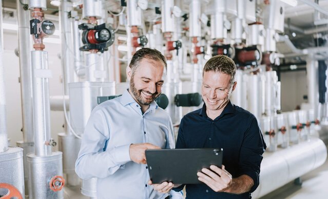 Zwei Männer stehen mit einem Tablet vor einer Heizung