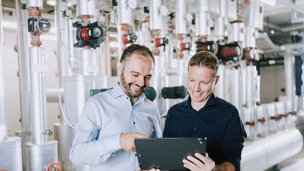 Zwei Männer stehen mit einem Tablet vor einer Heizung